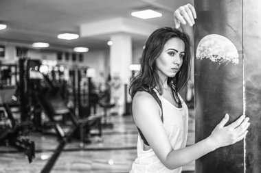 Siyah ve beyaz fotoğraf sportif kız spor salonunda boks torbası sarılma.