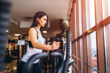 Spor salonunda eliptik eğitmen olarak çalışan çekici genç kadın 