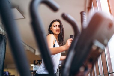 gülümseyen ve spor salonunda eliptik eğitmen olarak çalışma dışarı yorgun genç kadın 