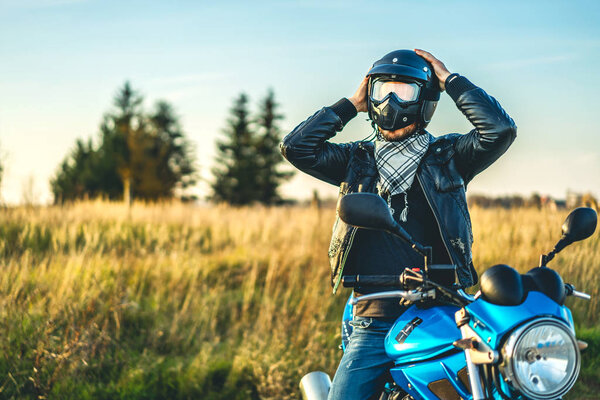 Biker putting helmet on head while sitting on sport motorcycle outdoor on road