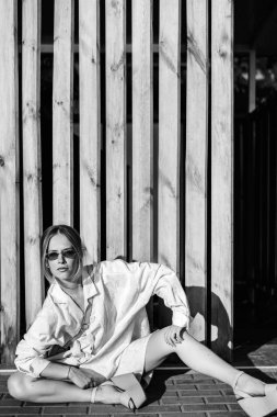 Tek renkli ahşap çit yakınında sokakta oturan moda kadın görünümünü