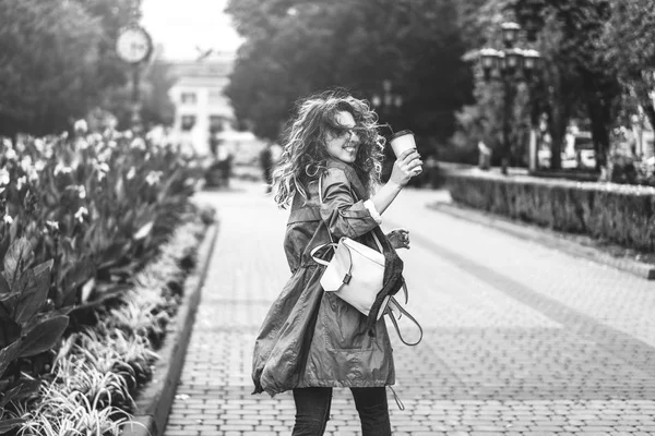 黒と白コーヒー カップと笑みを浮かべて 通りで歩いている巻き毛髪の少女 — ストック写真