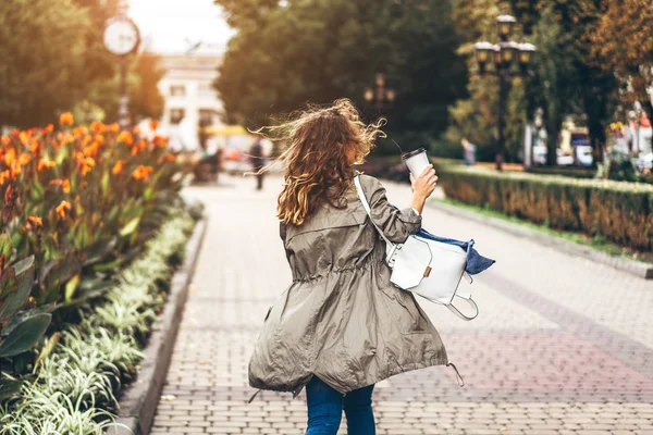 コーヒー カップが通りで歩いている巻き毛の女の子の背面図 — ストック写真