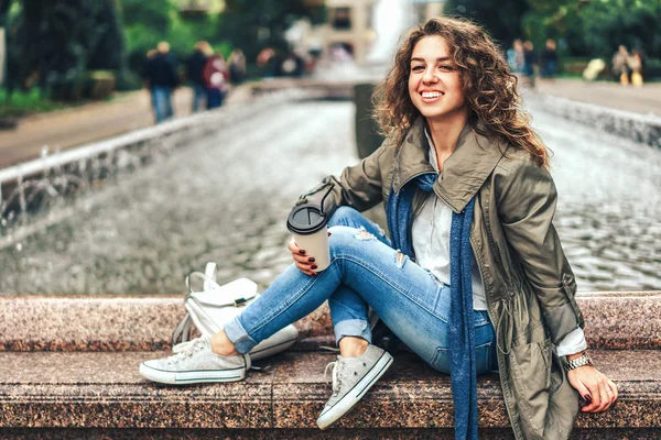 Meisje Met Krullend Haar Poseren Bij Fontein Met Koffiekopje Glimlachen — Stockfoto