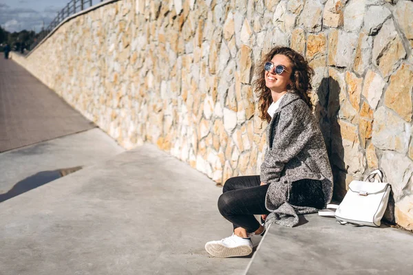 Güneş Gözlüğü Takıyor Taş Duvar Dibinde Poz Gülümsüyor Kıvırcık Saçlı — Stok fotoğraf