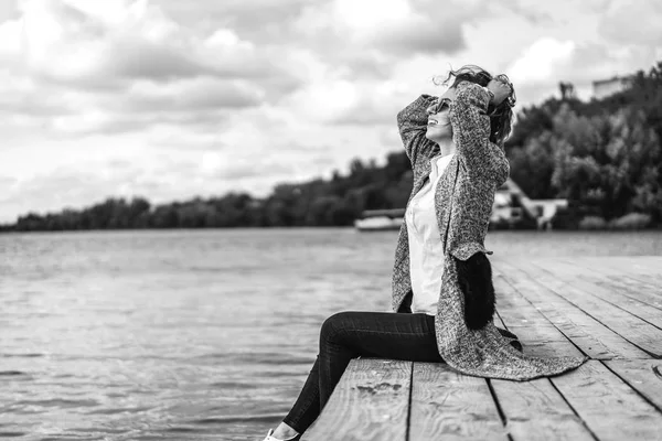 湖のそばにカーディガン座って押し髪 黒と白を身に着けている女の子 — ストック写真