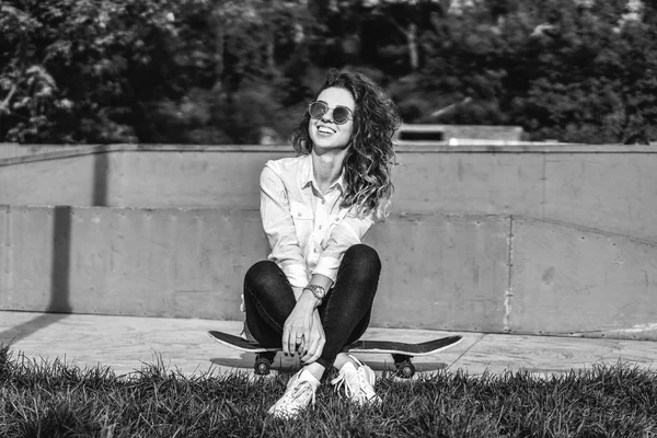 スケート ボードと笑っている 黒と白の上に座ってのサングラス巻き毛髪の少女 — ストック写真