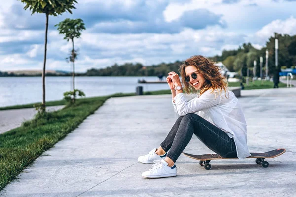 Hezká Dívka Kudrnatými Vlasy Sedí Skateboardu Parku Směje — Stock fotografie