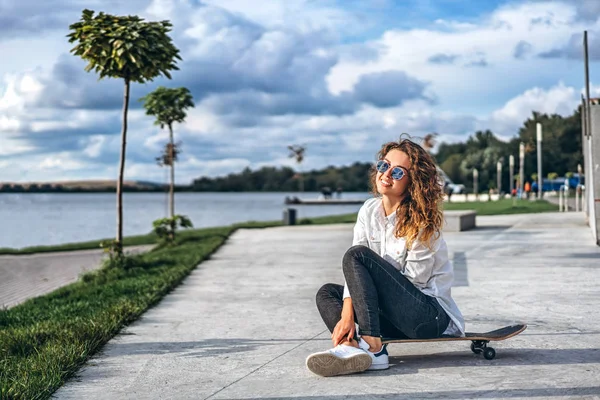 Hezká Dívka Kudrnatými Vlasy Sedí Skateboardu Parku Usmívá — Stock fotografie
