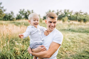 Çayır üzerinde yürürken ellerinde küçük oğlu taşıyan baba 