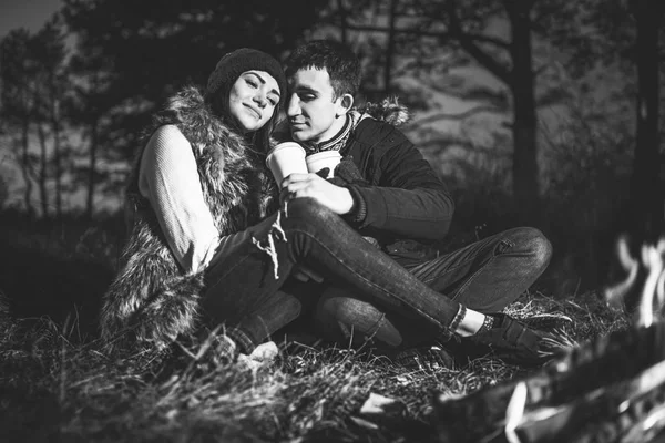 在篝火旁的森林里喝热饮料的漂亮年轻夫妇 — 图库照片