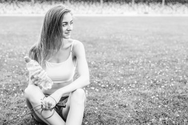 Oldukça sportif kız şişe su ile açık eğitim sonrası çimenlerin üzerinde rahatlatıcı.