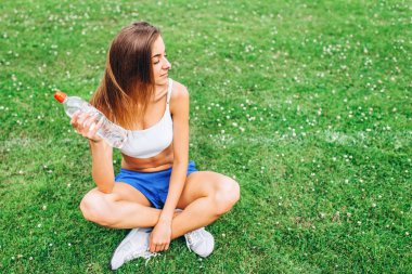 Oldukça sportif kız şişe su ile açık eğitim sonrası çimenlerin üzerinde rahatlatıcı.
