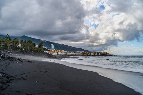 Landscape of mountains and ocean with cloudy sky and black beach