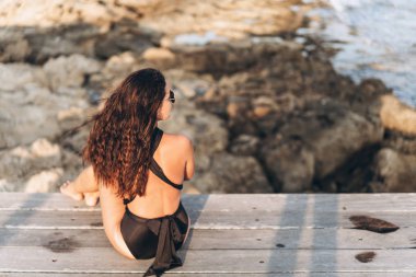 Güzel pan Asya kadın siyah mayo deniz kenarında iskelede rahatlatıcı