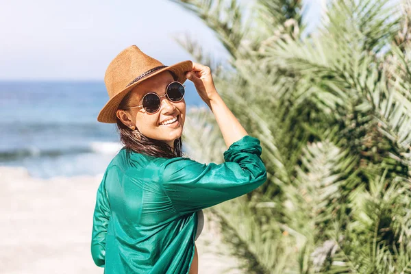 Cute pan asian girl in hat and sunglasses in green pareo walking on the seaside