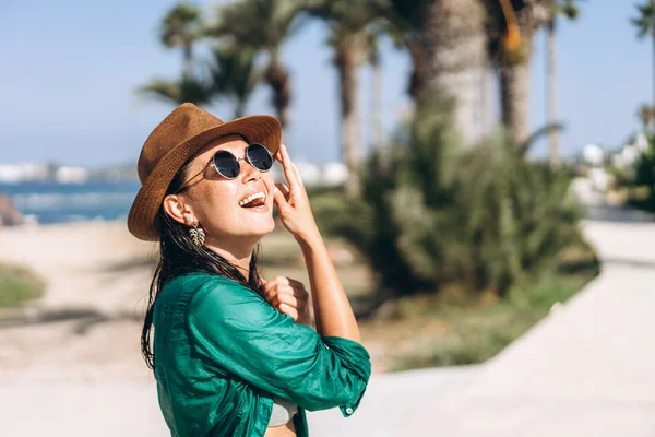 Schattig pan Aziatisch meisje in hoed en zonnebril in groene pareo wandelen — Stockfoto