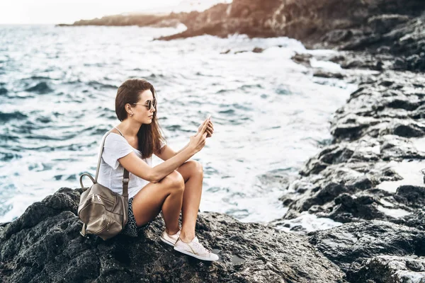 Oldukça uzun saç turist kız deniz kenarında taşlar üzerinde rahatlatıcı. — Stok fotoğraf