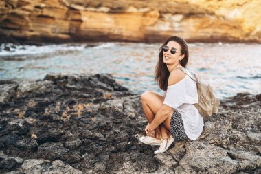 Oldukça uzun saç turist kız deniz kenarında taşlar üzerinde rahatlatıcı.