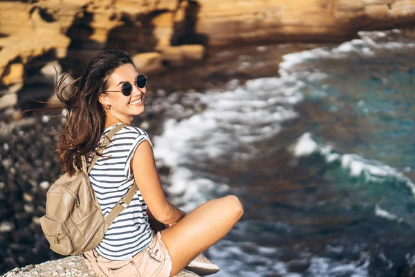 Piuttosto lunghi capelli ragazza turistica rilassante sulle pietre vicino al mare . — Foto Stock