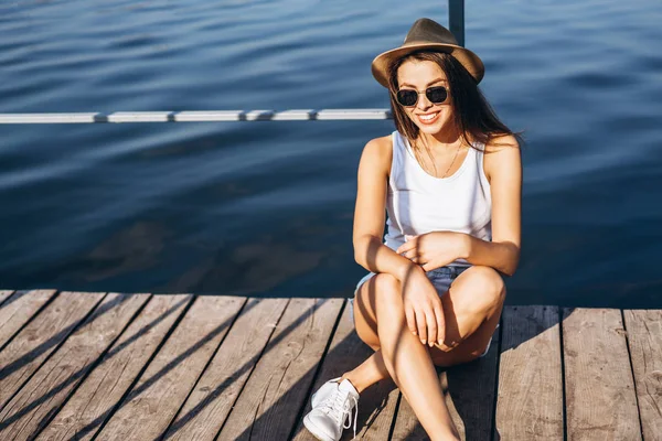 Schattig jong brunette meisje ontspannen op de pier in de buurt van meer. — Stockfoto