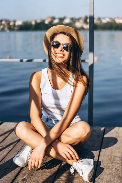 Schattig jong brunette meisje ontspannen op de pier in de buurt van meer. — Stockfoto