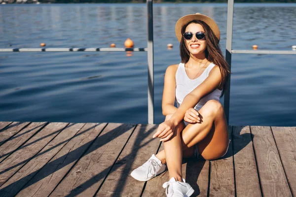 Schattig jong brunette meisje ontspannen op de pier in de buurt van meer. — Stockfoto