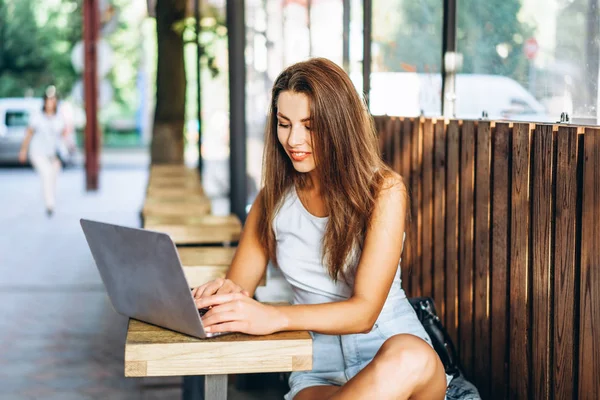 Hübsches junges Mädchen arbeitet auf Laptop in Straßencafé im Freien. — Stockfoto