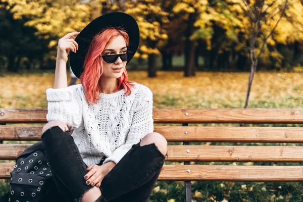 漂亮的女孩与红色的头发和帽子放松在长凳上 — 图库照片