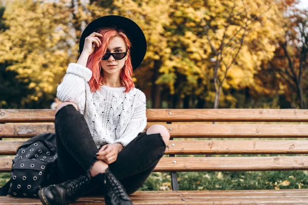 漂亮的女孩与红色的头发和帽子放松在长凳上 — 图库照片