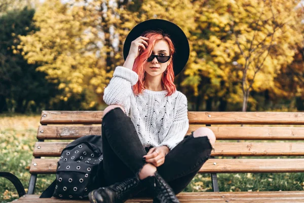 Bella ragazza con i capelli rossi e cappello rilassante sulla panca in p — Foto Stock