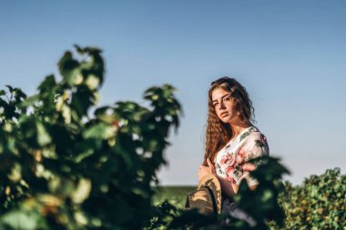 Frenk üzümü tarlasında uzun kıvırcık saçlı ve çilli güzel bir kadın. Hafif elbiseli bir kız yaz güneşli bir günde yürüyor..