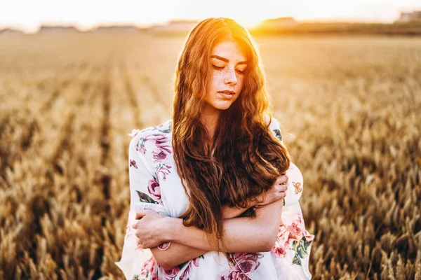 一个有着长长的卷发和雀斑脸的令人难以置信的年轻女人 日落时穿着衣服站在麦田里的女人 近景肖像 — 图库照片
