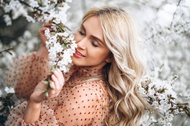 Muhteşem gülüşlü bir kadın çiçek açan bahçede eğleniyor. Doğal arka planda kırmızı elbiseli bir kadın, sağIık ve sakin bir konsept. Parkta kıvırcık sarı saçlı, şehvetli sarışın kız.