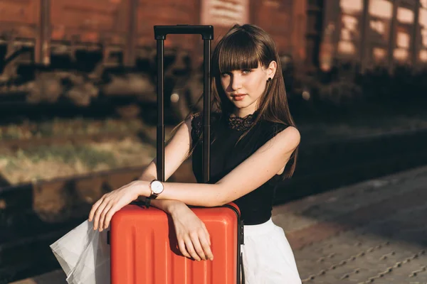 身穿白色短裙 头戴红色行李箱的女性黑发旅行者在候车站等火车 — 图库照片