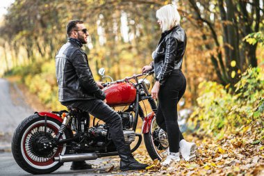Ormandaki yolda, kırmızı motorsikletin yanında, renkli, mavi arka planda güzel bir çift. İlişki kavramı.