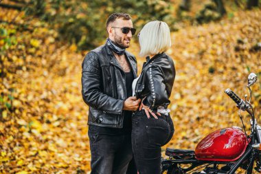 Ormandaki yolda, kırmızı motorsikletin yanında, renkli, mavi arka planda güzel bir çift. İlişki kavramı.