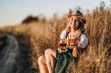 Kızların elleri dirndl 'de, geleneksel festival elbisesi içinde, kocaman köpüklü bir bardak bira doldururken, arka planda bulanıklık var. Ekim Festivali, Aziz Patrick Günü, uluslararası bira günü konsepti
