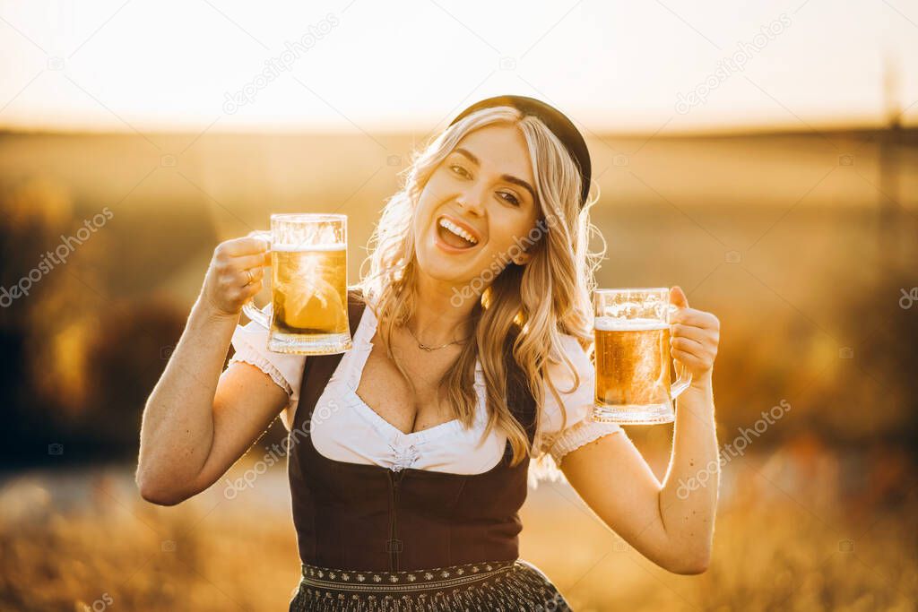 Close-up of the girls hands in dirndl, traditional festival dress, pouring a full glass of beer with huge foam, outdoors with blurred background. Oktoberfest, St Patricks day, international beer day concept