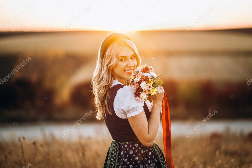 Close-up of the girls hands in dirndl, traditional festival dress, pouring a full glass of beer with huge foam, outdoors with blurred background. Oktoberfest, St Patricks day, international beer day concept