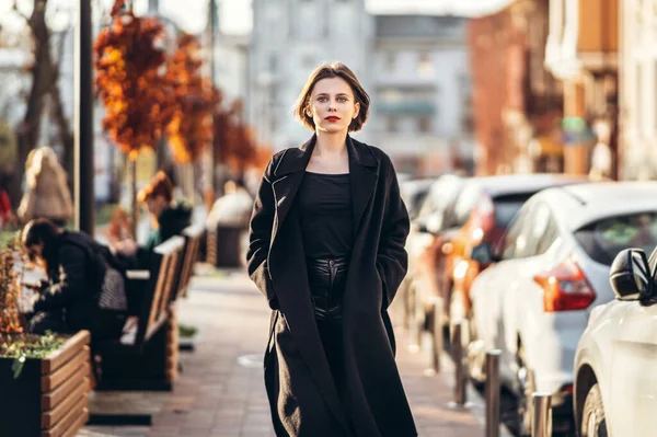 一个短发的年轻女人 穿着一件黑色的外套 漫步在城市的街道上 周围都是人和汽车 一个女人看着摄像机 — 图库照片
