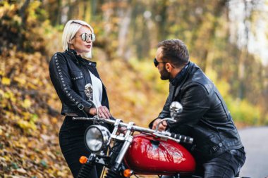 Ormandaki yolda, kırmızı motorsikletin yanında, renkli, mavi arka planda güzel bir çift. İlişki kavramı.