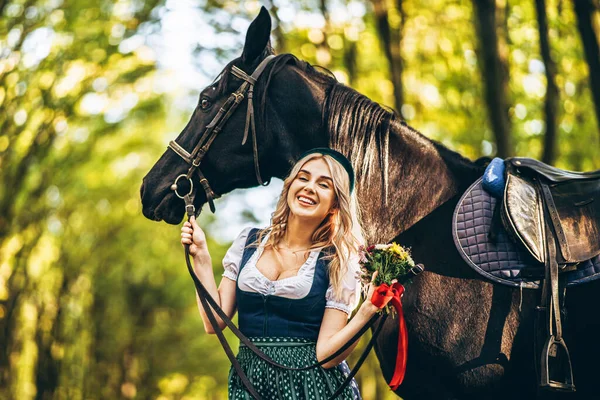 Ładna Blondynka Tradycyjnej Sukience Spacerująca Dużym Czarnym Koniem Lesie Koncepcja — Zdjęcie stockowe