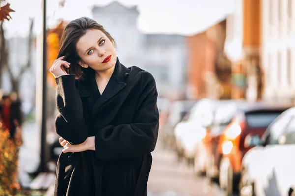 一个留着短发和红唇的年轻女人 穿着一件黑色外套 漫步在城市的街道上 周围都是人和车 — 图库照片