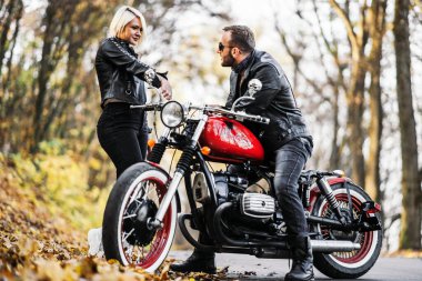 Ormandaki yolda, kırmızı motorsikletin yanında, renkli, mavi arka planda güzel bir çift. İlişki kavramı.