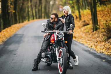 Ormandaki yolda, kırmızı motorsikletin yanında, renkli, mavi arka planda güzel bir çift. İlişki kavramı.