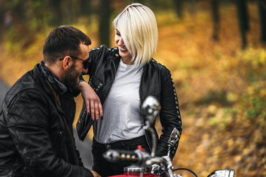 Ormandaki yolda, kırmızı motorsikletin yanında, renkli, mavi arka planda güzel bir çift. İlişki kavramı.