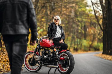 Ormandaki yolda, kırmızı motorsikletin yanında, renkli, mavi arka planda güzel bir çift. İlişkiler kavramı.