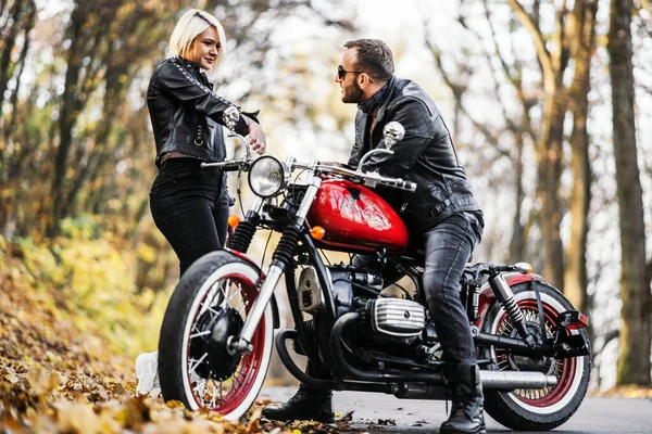 Ormandaki yolda, kırmızı motorsikletin yanında, renkli, mavi arka planda güzel bir çift. İlişki kavramı.