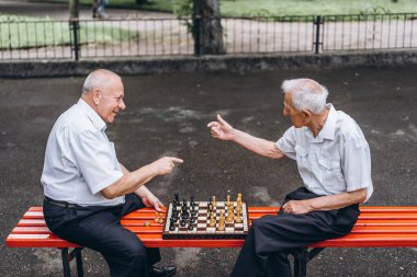 Parktaki bankta satranç oynayan iki yetişkin adam.